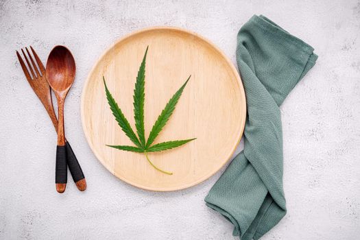 Food conceptual image of a cannabis leaf  with spoon and fork on white concrete background.