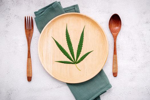 Food conceptual image of a cannabis leaf  with spoon and fork on white concrete background.