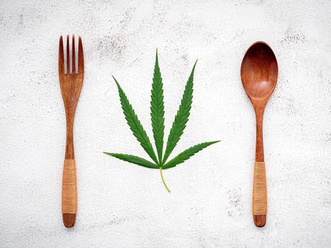 Food conceptual image of a cannabis leaf  with spoon and fork on white concrete background.