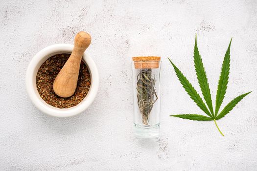 Glass bottle of cannabis oil with white mortar and hemp leaves set up  on concrete background.