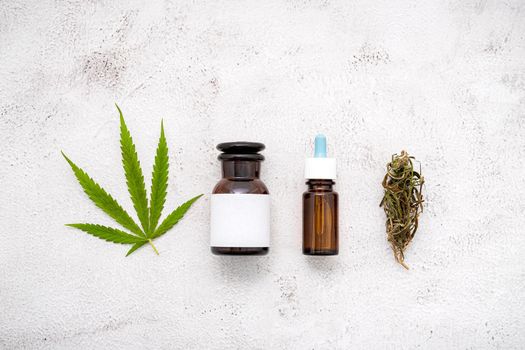 Glass bottle of cannabis oil with white mortar and hemp leaves set up  on concrete background.