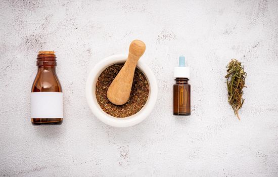 Glass bottle of cannabis oil with white mortar and hemp leaves set up  on concrete background.