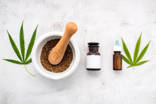 Glass bottle of cannabis oil with white mortar and hemp leaves set up  on concrete background.