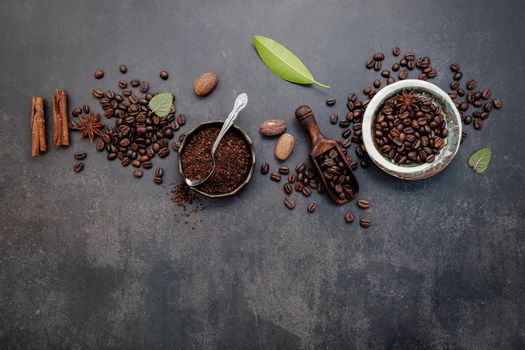 Roasted coffee beans with coffee powder and flavourful ingredients for make tasty coffee setup on dark stone background.