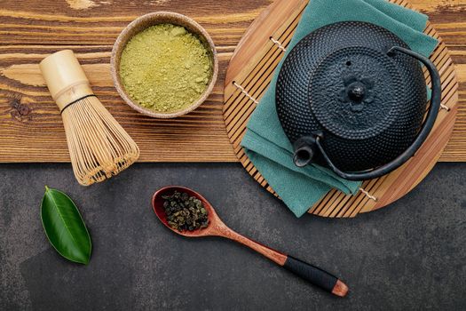 Black cast iron tea pot with herbal tea set up on dark stone background.