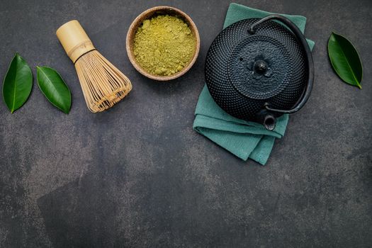 Black cast iron tea pot with herbal tea set up on dark stone background.