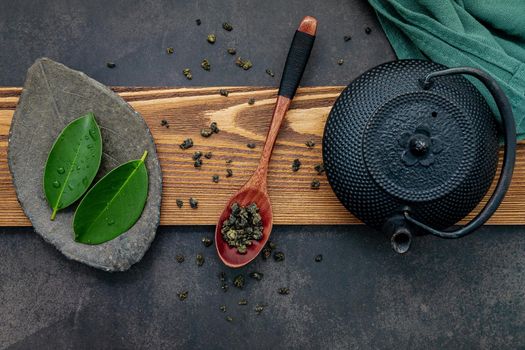 Black cast iron tea pot with herbal tea set up on dark stone background.