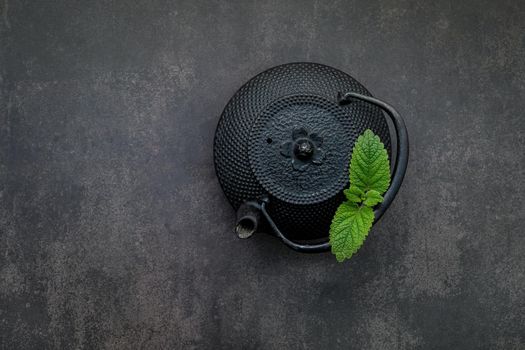 Black cast iron tea pot with herbal tea set up on dark stone background.