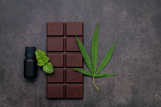 Food conceptual image of  cannabis leaf  with dark chocolate and fork on dark concrete background.