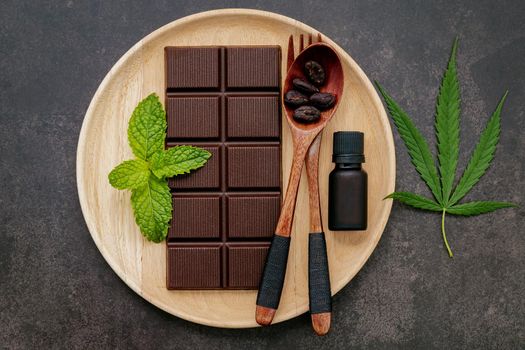 Food conceptual image of  cannabis leaf  with dark chocolate and fork on dark concrete background.