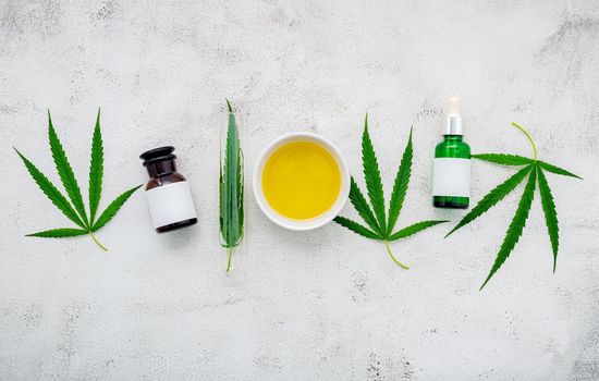 Glass bottle of cannabis oil and hemp leaves set up  on concrete background.