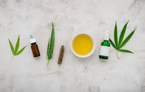 Glass bottle of cannabis oil and hemp leaves set up  on concrete background.