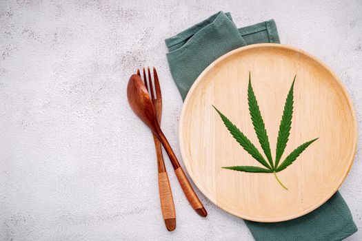 Food conceptual image of a cannabis leaf  with spoon and fork on white concrete background.