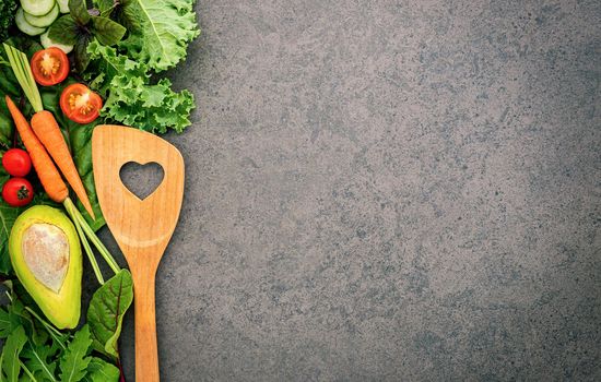 Healthy food and cooking concept wooden spatula and vegetables on dark stone background.