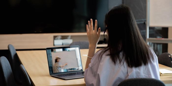 Asian young girl student learning virtual internet online class from school teacher by remote meeting due to covid pandemic. Female teaching by using headphone and whiteboard.