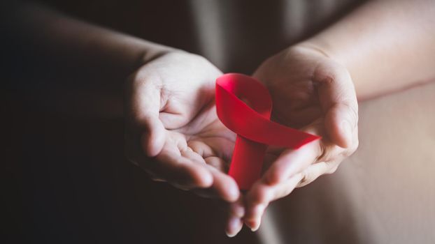 World AIDS day awareness ribbon,Female hands holding red ribbon HIV,Healthcare and medicine concept.