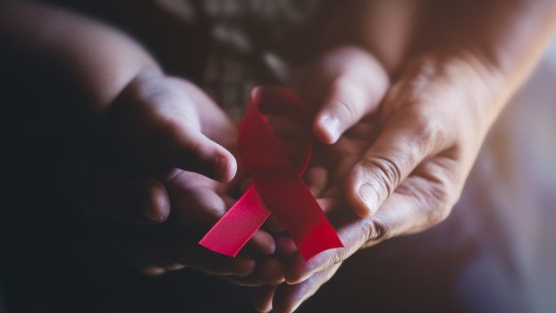 Adult and child hands holding red ribbon, hiv awareness concept, world AIDS day, world cancer day, world hypertension day