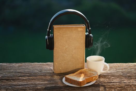 Audio book concept. Headphones and old book with breakfast on wooden
