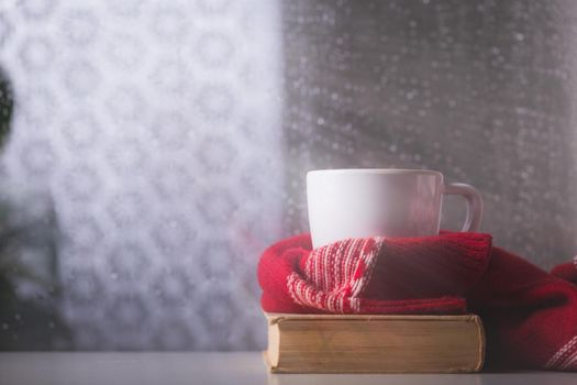 Cup of tea or coffee and some books on the table in front of the window. Rainy and cold day outside, reading, autumn mood