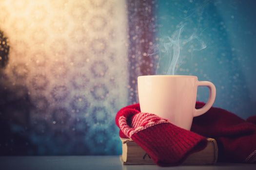 Cup of tea or coffee and some books on the table in front of the window. Rainy and cold day outside, reading, autumn mood