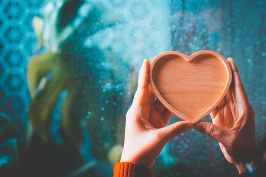 Woman's hand holding a wooden heart on a rainy background. Valentines Day concept.