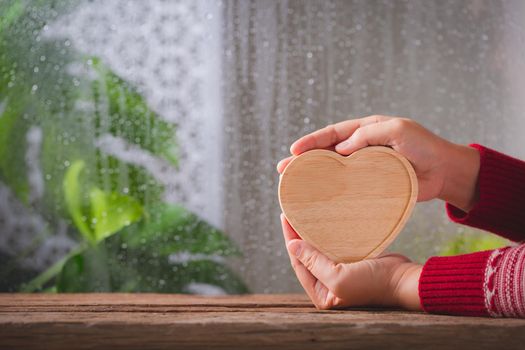 Woman hand holding wooden heart on rainy background, Valentine day concept