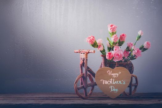 Still life with sweet carnation flowers in wood bicycle on wooden table, Mothers day concept With a message for Happy Mother's Day on a wooden heart
