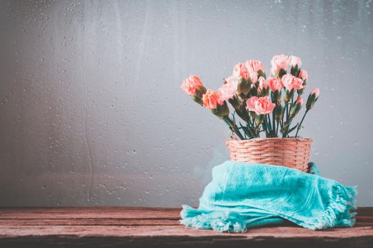 Still life with sweet carnation flowers in basket beside window on wooden table