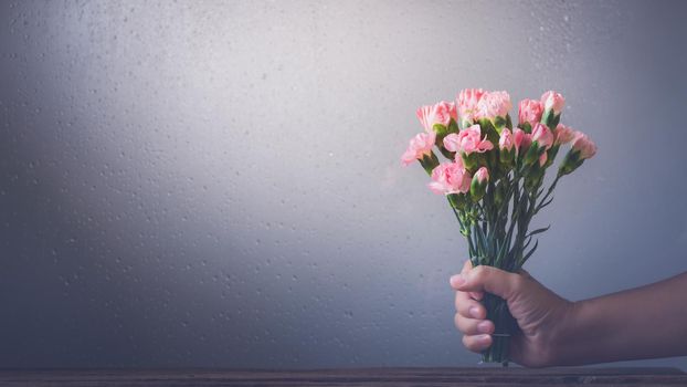 Still life with sweet carnation flowers in hand  beside window on wooden table