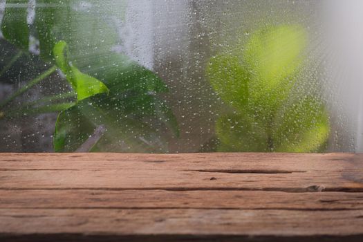 Wooden table near window on rainy day with tropical plant