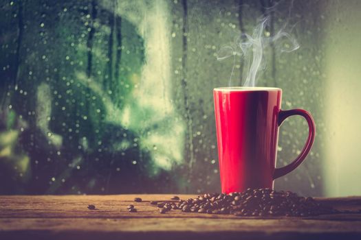 Red cup of coffee beside window and the rain on tropical plant background