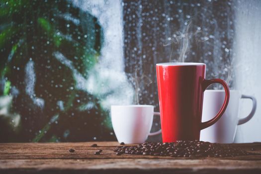 Red cup of coffee beside window and the rain on tropical plant background