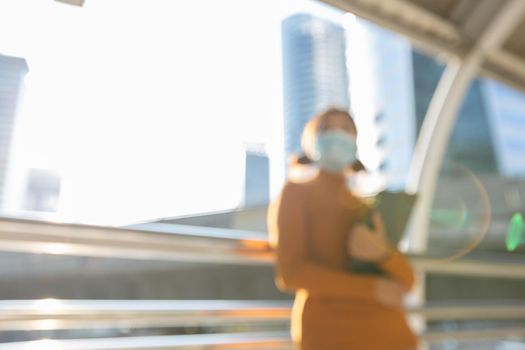 Blurred woman wearing a mask to the sunny city of the morning, Abstract background