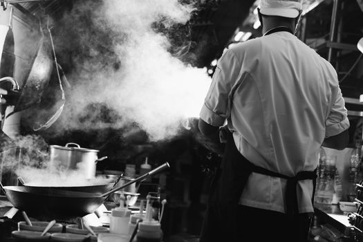 Chef stir fry busy cooking in kitchen. Chef stir fry the food in a frying pan, smoke and splatter the sauce in the kitchen., Black and white