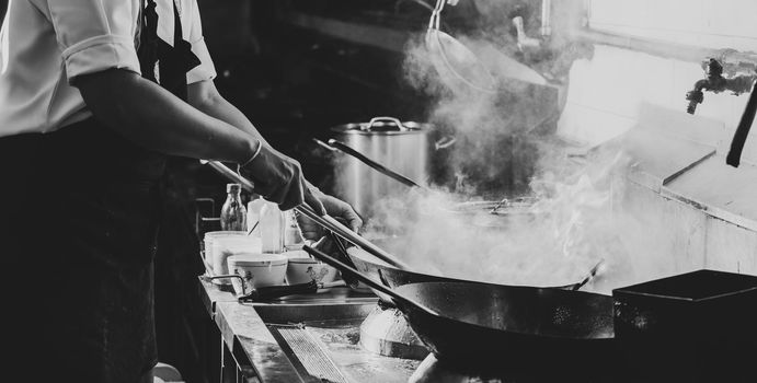 Chef stir fry busy cooking in kitchen. Chef stir fry the food in a frying pan, smoke and splatter the sauce in the kitchen., Black and white