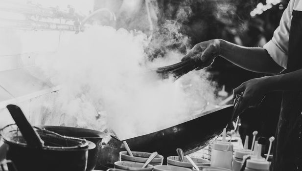 Chef stir fry busy cooking in kitchen. Chef stir fry the food in a frying pan, smoke and splatter the sauce in the kitchen., Black and white