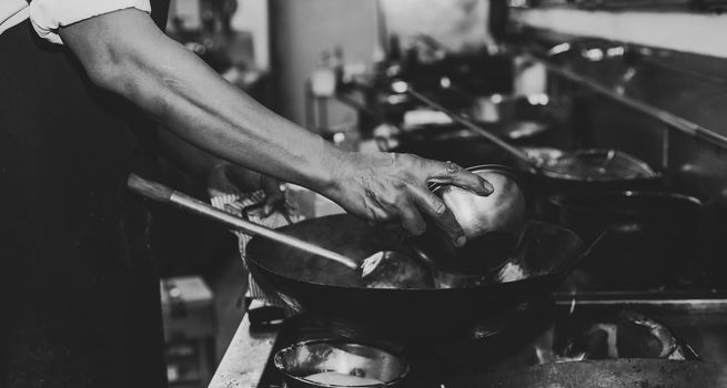 Chef stir fry busy cooking in kitchen. Chef stir fry the food in a frying pan, smoke and splatter the sauce in the kitchen., Black and white