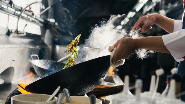 Chef stir fry busy cooking in kitchen. Chef stir fry the food in a frying pan, smoke and splatter the sauce in the kitchen.