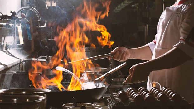 Chef stir fry busy cooking in kitchen. Chef stir fry the food in a frying pan, smoke and splatter the sauce in the kitchen.
