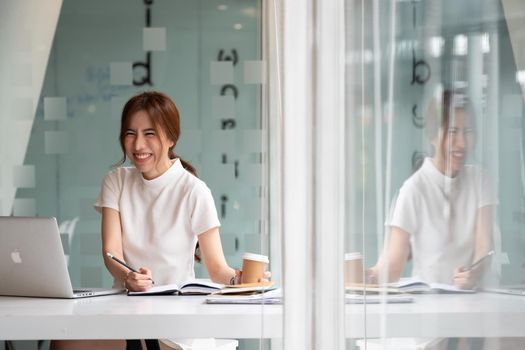 Attractive smiling young asian woman working in the office with laptop computer