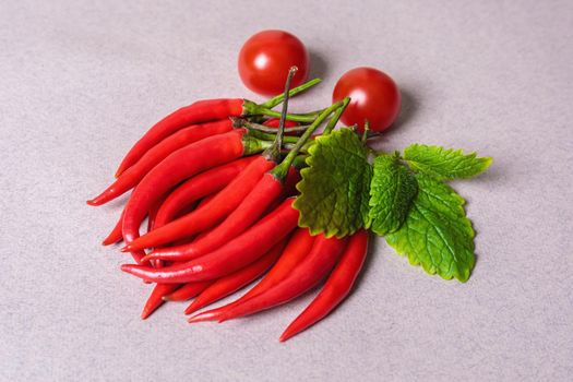 Slide of red chili peppers with one red tomato on a light background. View from above.