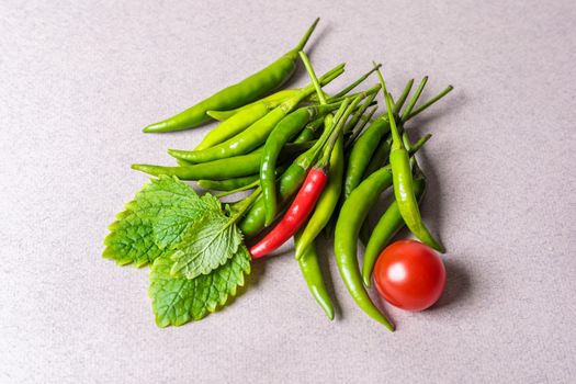Slide of green chili peppers with one red tomato on a light background. View from above.