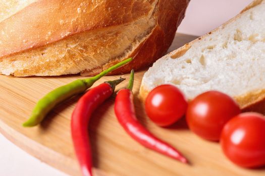 Sliced pieces of white bread with red peppers and tomatoes on a cutting board. Light background