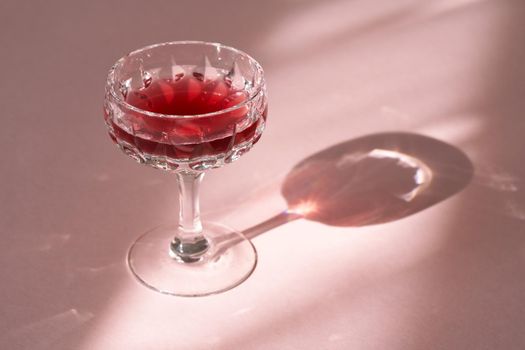 A glass of black elder syrup with water on pink background with shadows