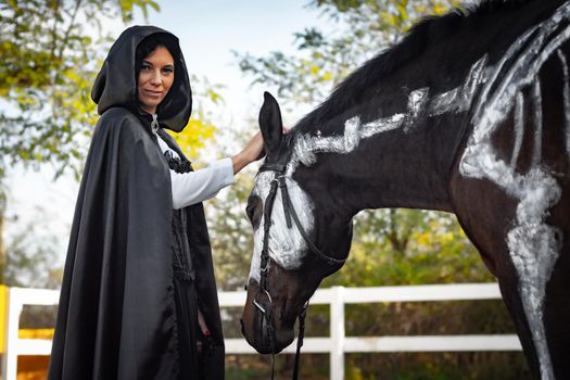 Portrait of a beautiful girl dressed in medieval style, a horse with a painted skeleton is standing next to