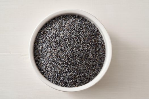 Poppy seeds in a bowl on a white wooden background, top view