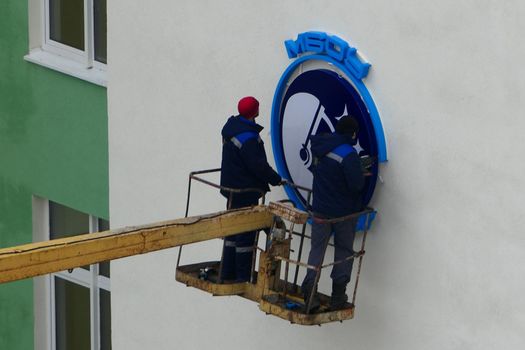 A team of workers mount a sign on the facade of the building with the help of special equipment at altitude. High quality photo