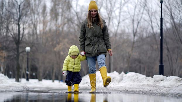 Mom and daughter walking in a puddle in yellow rubber boots.