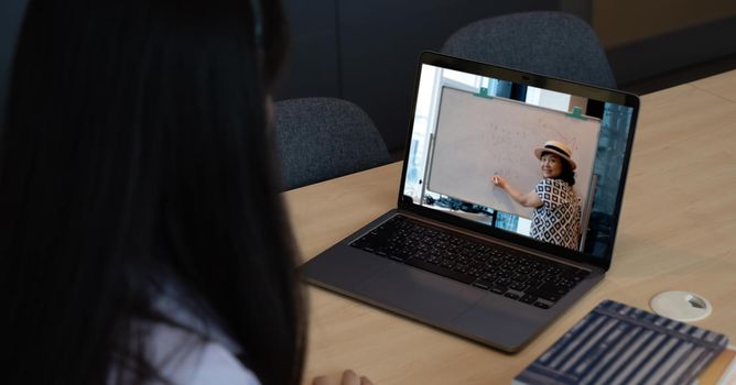 Asian young girl student learning virtual internet online class from school teacher by remote meeting due to covid pandemic. Female teaching by using headphone and whiteboard.