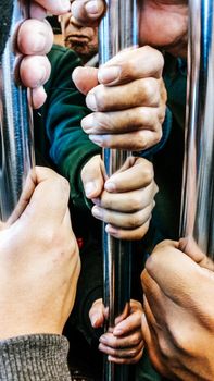 Closeup, people hands holding handrail inside the train.